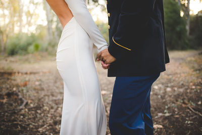 Midsection of bride and groom holding hands and standing on field