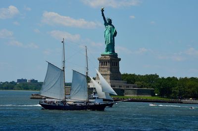Boats sailing on sea by statue of liberty against sky