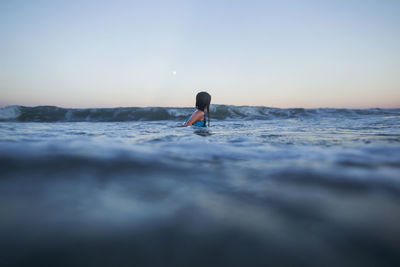 Woman swimming in sea against clear sky during sunset
