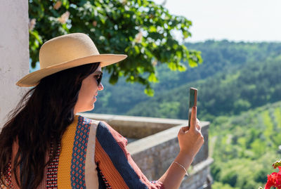 Woman standing on terrace of old building, taking photos of beautiful landscape