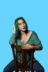 Young woman sitting on chair against blue background