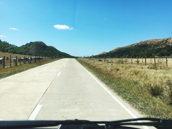 Empty road amidst field against sky