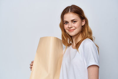 Portrait of smiling woman holding paper bag against gray background