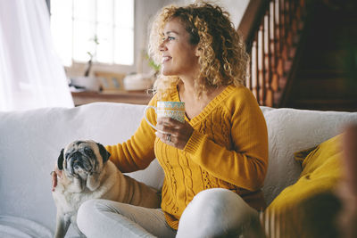 Smiling woman holding coffee cup sitting with dog at home