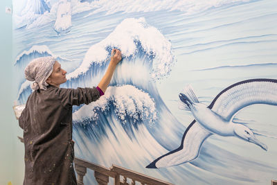 Mature woman artist draws a mural on a marine theme