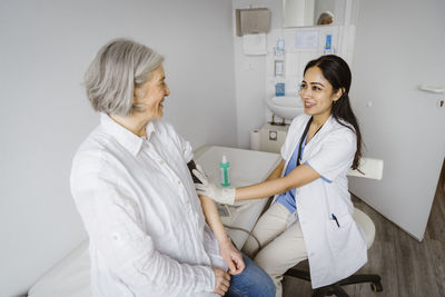 Smiling female healthcare worker consulting senior patient in examination room at clinic