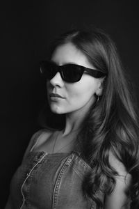 Portrait of young woman wearing sunglasses against black background
