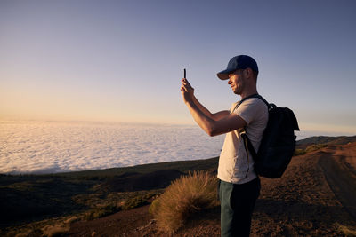 Concentrated man photographing landscape above clouds. tourist enjoy at beautiful sunset. 
