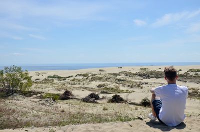 Rear view of man sitting on beach against sky