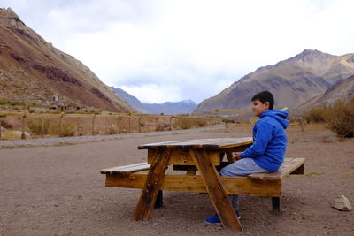 Side view of man sitting on seat against mountains