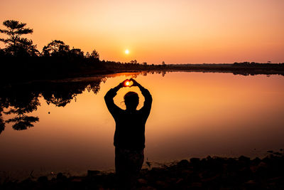 Silhouette man standing by lake against sky during sunset