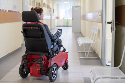 Rear view of woman sitting on wheelchair in hallway