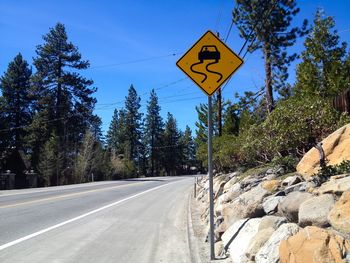 Road sign by trees against blue sky