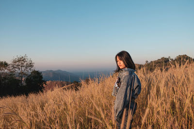 Young woman standing on field against sky during sunset