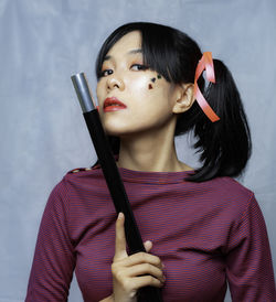 Portrait of woman holding camera against wall