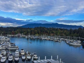 Boats moored at harbor by lake against sky