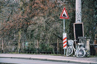 Old bicycle and information sign on sidewalk against trees