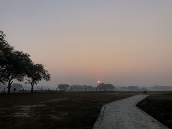 Footpath amidst field against clear sky during sunset