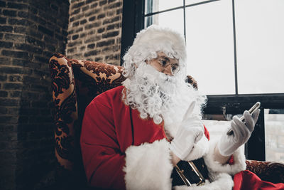 Man wearing santa claus costume using phone on sofa at home