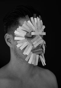 Close-up of shirtless man with papers on face against black background