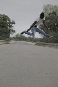 Man jumping on road against clear sky