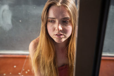 Portrait of young woman looking through window