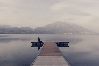 Man on pier on lake against sky