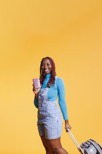 Young woman drinking milk while standing against yellow wall