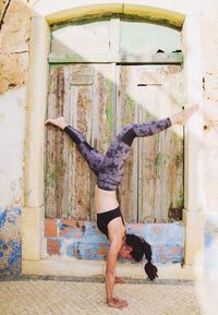 Woman practicing handstand at entrance of old house