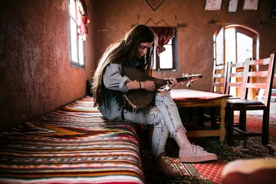 Woman playing musical instrument while sitting on bed at home