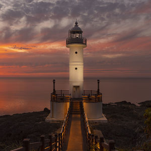 Lighthouse by sea against sky during sunset