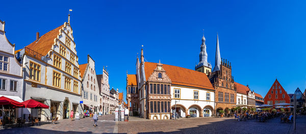 People on street amidst buildings in city against clear blue sky