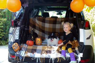 Cute girl sitting with dog in car trunk