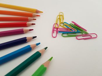 High angle view of colored pencils and paper clips arranged on gray background