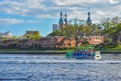 Boats in river by buildings against sky