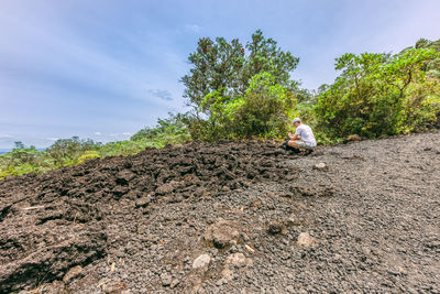 Side view of man crouching on hill against sky