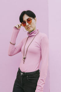 Woman wearing sunglasses standing in front of pink wall