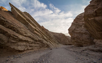 Dirt road passing through rock formation against sky