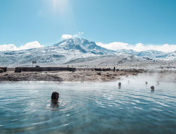 People swimming in pool by snowcapped mountains against sky