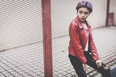 Portrait of young woman standing against fence
