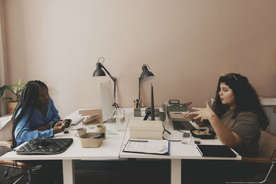 Female business colleagues discussing during lunch break while sitting at desk in office