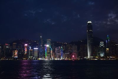 Illuminated buildings by river against sky at night