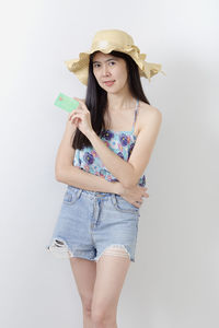 Portrait of young woman holding hat against white background