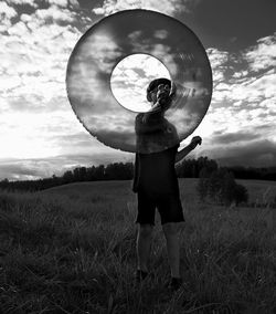 Rear view of a kid standing on field, holding a transparent swimming ring. 