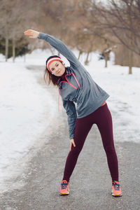 Full length portrait of woman exercising on road during winter