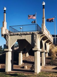 Low angle view of flags on bridge against blue sky
