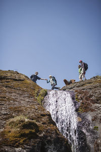 Low angle view of friends hiking on mountain against clear sky