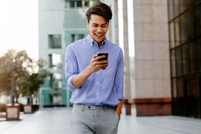 Smiling young man using mobile phone while standing on laptop