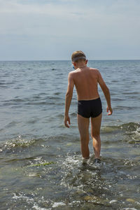 Ten-year-old boy in gray swimming trunks enters the sea water