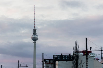 Communications tower in city against cloudy sky